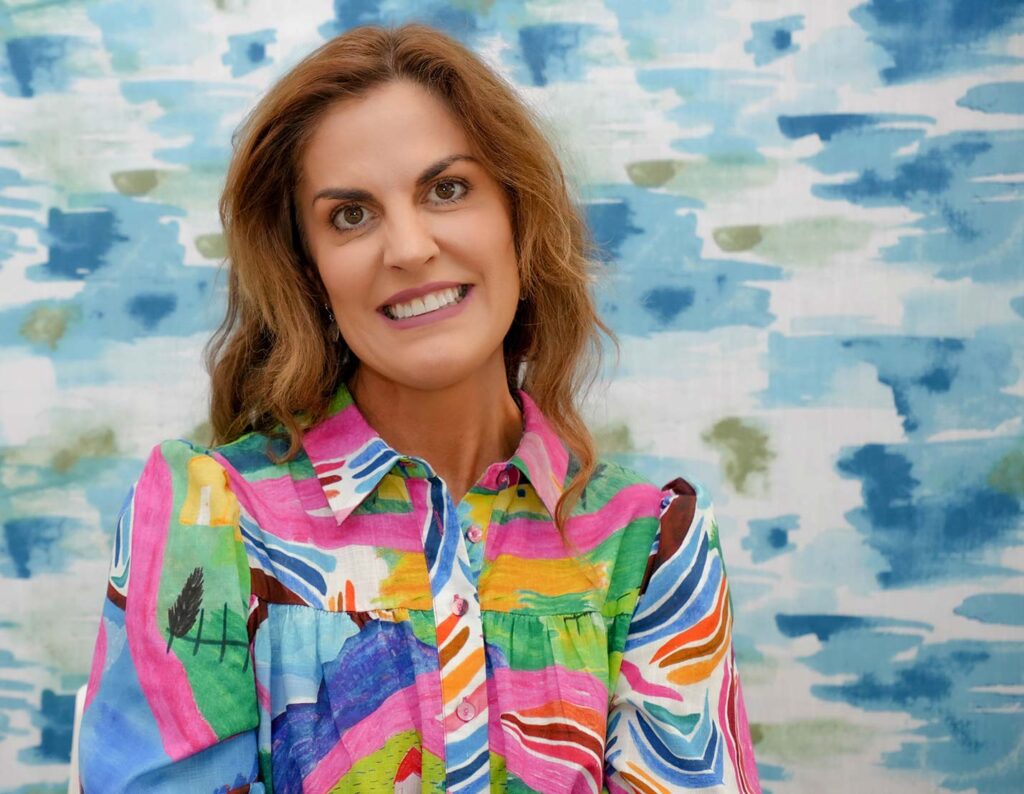 A smiling woman wearing a colourful, patterned shirt.