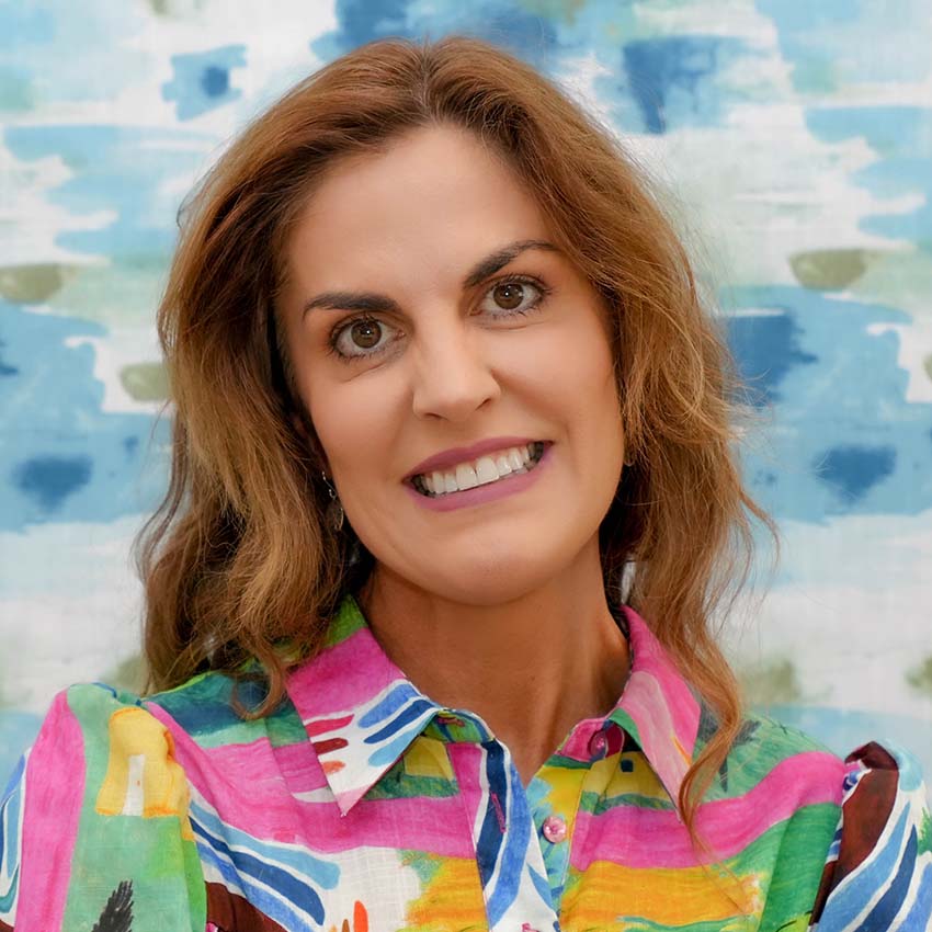 Katrina-Bell-cropped Portrait of a smiling woman in a colourful patterned shirt.