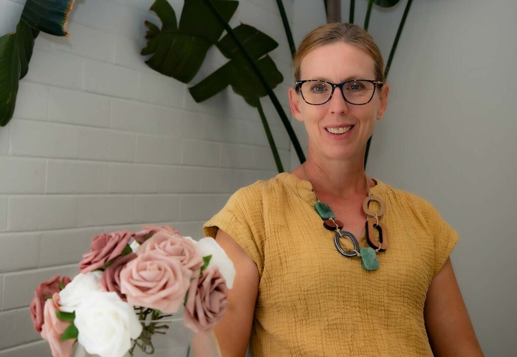 Smiling woman in yellow top behind pink and white roses.